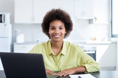 Neşeli, kısa saçlı, iş yerinde laptopuyla oturan, kameraya bakan, gülümseyen kısa saçlı siyahi bir iş kadını. Milenyum çalışanı, çalışanı, girişimci portresi