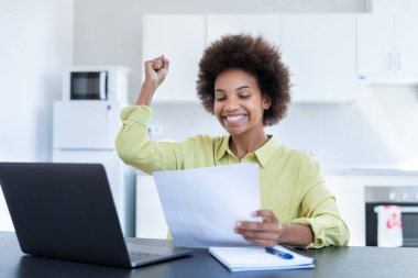 Mutlu gülümseyen, çalışan, uzaktan kumandalı genç zenci kadın şirket ofisinden proje raporu onayı için posta alıyor. Bin yıllık Afro-Amerikan çalışanın kağıt dökümanından iyi haberler okumasına sevindim.