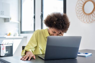 Stresli genç Black serbest çalışan kadın migrenden muzdarip, iş yerinde baş ağrısı çekiyor. Afrikalı çalışan, ev işçisi, iş kadını dizüstü bilgisayarda oturuyor, tapınaklara dokunuyor, kafa tutuyor..