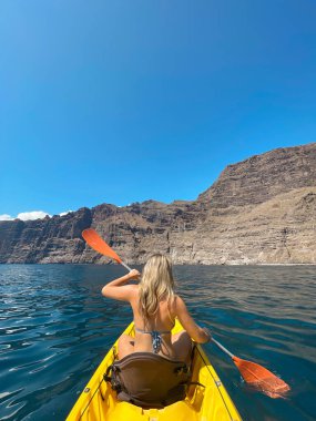Mutlu ve güzel sarışın bir kadın açık denizde kanoyla kürek çekiyor ve eğleniyor. Yaz tatilinde sahilde eğleniyoruz..