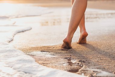 Plaj gezisi. Kumsalda yürüyen bir kadın. Kumda ayak izleri bırakıyor. Tenerife sahilinde kadın ayağı ve altın kumun yakın çekimi..