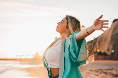 Plajda kollarını açmış, boş zamanın ve dışarıda özgürlüğün tadını çıkaran genç bir kadının portresi. Rahatlamak ve mutlu anlar yaşamak..