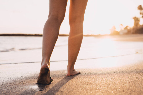 Пляжные путешествия - женщина, идущая по песчаному пляжу, оставляя следы на песке. Детали крупным планом женских ног и золотой песок на пляже Тенерифе.