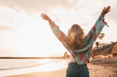 Sarışın bir kadının kumsalda yürüyüp günbatımının tadını çıkarışını. 