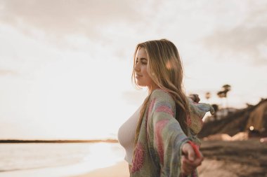 Kumsalda mutlu sarışın kadın, günbatımı gökyüzü ve arka planda bulanık deniz. 