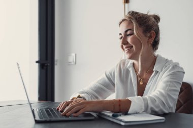 Evde bilgisayarla çalışan mutlu ve serbest bir genç kadın. Çevrimiçi öğrenim gören çekici iş kadını, dizüstü bilgisayar, web sörfü bilgileri veya internet mağazasından alışveriş yapıyor..
