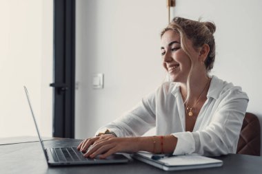 Evde bilgisayarla çalışan mutlu ve serbest bir genç kadın. Çevrimiçi öğrenim gören çekici iş kadını, dizüstü bilgisayar, web sörfü bilgileri veya internet mağazasından alışveriş yapıyor..