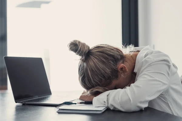 Exhausted young Caucasian female employee sleep desk at office overwork preparing report. Tired woman fall asleep doze off at workplace, work late to meet deadline. Fatigue, exhaustion concept.