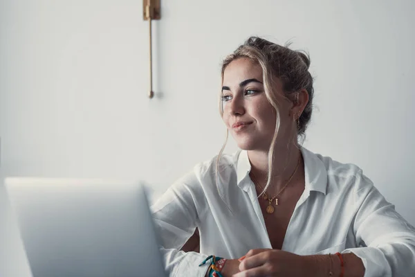 stock image Thoughtful millennial student girl sitting at table with laptop, open books, looking away, thinking over training course, learning webinar, online lesson, test. Elearning, distance work from home