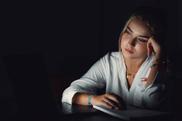 Уставшая молодая женщина сидит за рабочим столом после окончания рабочего дня в одиночестве в массажных храмах, пытаясь вспомнить важную информацию. Уставшая женщина-работница чувствует головную боль, вызванную работой сверхурочно