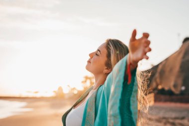 Plajda kollarını açmış, boş zamanın ve dışarıda özgürlüğün tadını çıkaran genç bir kadının portresi. Rahatlamak ve mutlu anlar yaşamak..