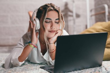 Evde dizüstü bilgisayar kullanan, kulaklık takıp müzik dinleyen genç ve mutlu bir kadını yakından çek. Milenyum gençleri gözleri kapalı şarkıların tadını çıkarıyor.