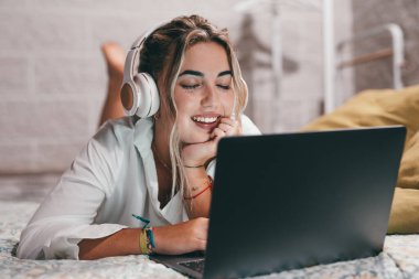 Evde dizüstü bilgisayar kullanan, kulaklık takıp müzik dinleyen genç ve mutlu bir kadını yakından çek. Milenyum gençleri gözleri kapalı şarkıların tadını çıkarıyor.