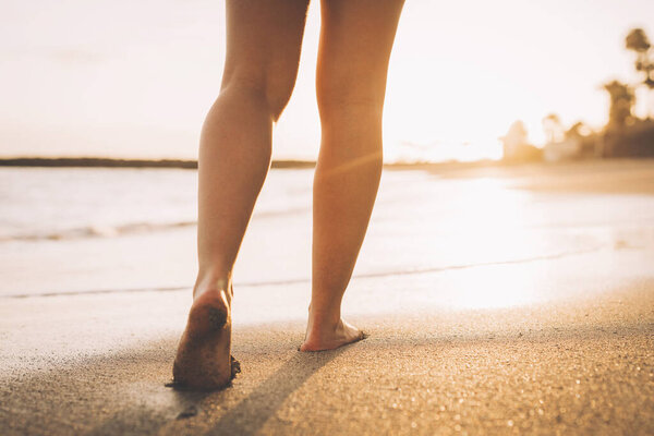 Пляжные путешествия - женщина, идущая по песчаному пляжу, оставляя следы на песке. Детали крупным планом женских ног и золотой песок на пляже Тенерифе.