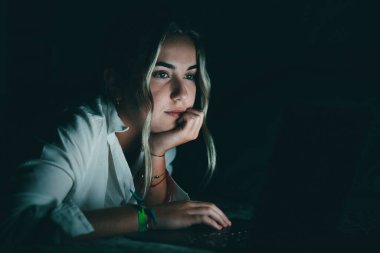 Kendine güvenen beyaz öğrenciyi gece yatakta dizüstü bilgisayar kullanarak, geç saatlerde çalışarak, son teslim tarihinde, bilgisayar ekranına bakarak, üniversite ödevleri için yatak odasında oturarak kapat.