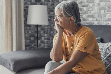 Face of senior caucasian hoary woman looking away deep in sad thoughts feels lonely close up portrait, recollect memories and life moments, depressed grandmother alone indoors, yearning for husband concept