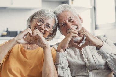 Yakın portre mutlu orta yaşlı aile samimi orta yaşlı çift parmakları ile kalp jesti, sevgi göstermek ya da kapalı alanda samimi duygular göstermek, kameraya bakarak.