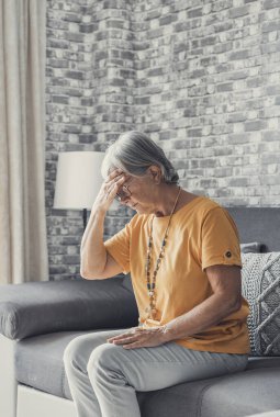 Üzgün, orta yaşlı, olgun bir kadın evde tek başına oturuyor, baş ağrısı çekiyor, migren ağrısı çekiyor, yaşlı ve üzgün bir kadın dul yas tutuyor, kederli, yalnız, zihinsel sorunlar yaşıyor.