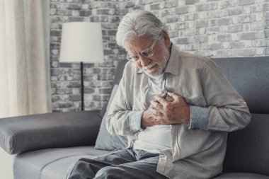 Worried elder senior man feeling bad, upset old middle aged grandfather touching chest feel sudden pain heartburn having heart attack sit on sofa at home clipart