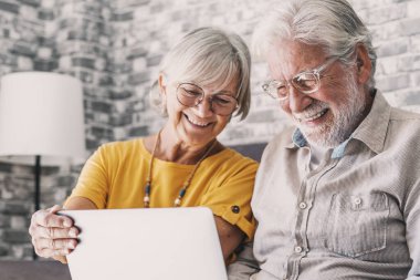 70 'lerin oldukça yaşlı gri saçlı çifti oturma odasında kanepede dinleniyor dizüstü bilgisayarda oturup gülümseyen film izliyorlar boş zamanın, eski neslin ve modern kablosuz teknolojinin keyfini çıkarıyorlar.