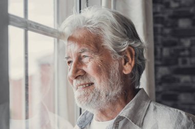 Mutlu, düşünceli 70 'lerin yaşlı adamı umutla pencereden dışarı bakıyor, sağlık, emeklilik, sigorta primleri, geleceği hayal ediyor. Yaşlı emekliler aile toplantısını bekliyor.