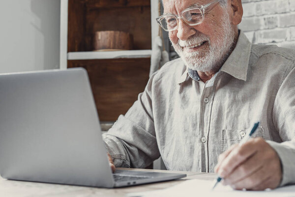 Aged remote worker. Concentrated senior male in glasses work on laptop from home office read email electronic document. Old age man employee freelancer sit at kitchen table by pc typing report online