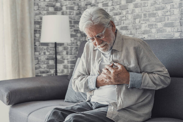Worried elder senior man feeling bad, upset old middle aged grandfather touching chest feel sudden pain heartburn having heart attack sit on sofa at home