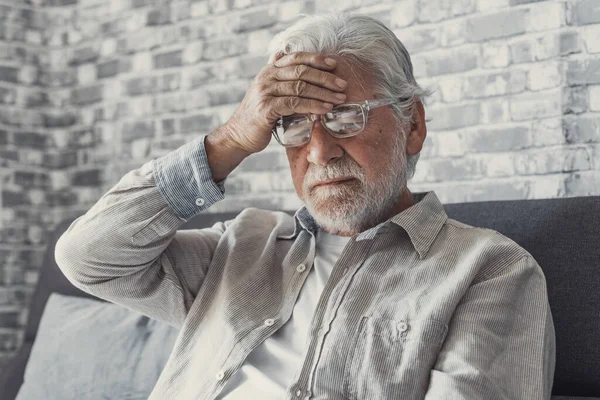 stock image Frustrated unhealthy senior mature man touching head, having painful feelings sitting alone at home. Unhappy middle aged retired grandfather suffering from high blood pressure disease indoors.