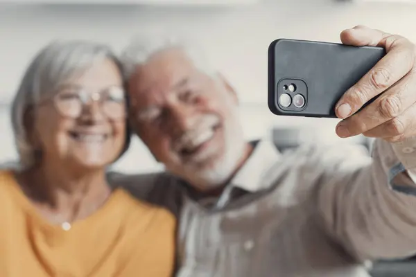 Happy old couple taking selfie on cellphone, smiling senior mature spouses middle aged wife and retired husband laughing holding phone make self portrait on smartphone camera, focus on mobile display
