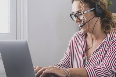 Çekici beyaz kadın, ofiste kulaklık takarak oturuyor ve dizüstü bilgisayar kullanılarak eğitici bir web sitesinde yer alıyor. Müşterilerle video görüşmesi ya da arkadaşlarla kişisel sohbet konsepti