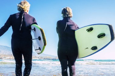 happy and healthy seniors enjoying summer and vacations outdoors at the beach entering to the water with wetsuits and surfboards - pensioners and retired go surfing clipart