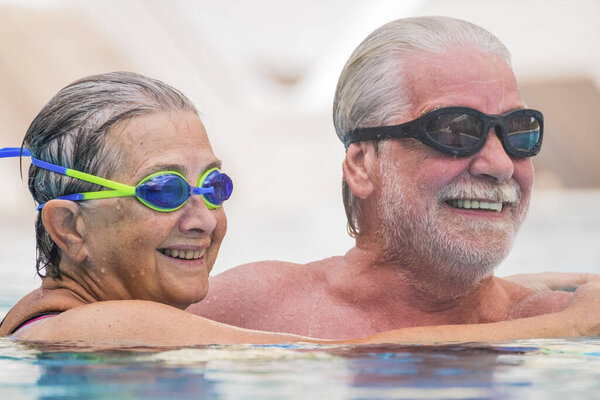 beautiful couple of two seniors together at the swimming pool having fun - woman hugged at her husband smiling with love