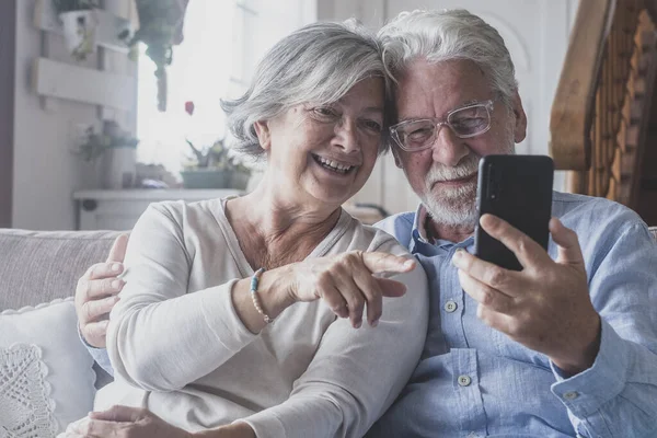 Smiling sincere mature older married family couple holding mobile video call conversation with friends, enjoying distant communication with grown children, using smartphone applications at home.