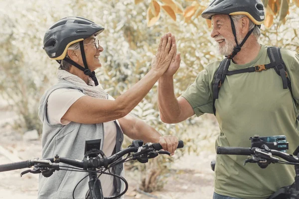 Couple of two seniors giving five together outdoors having fun with bicycles enjoying nature. Couple of old people building a healthy and fit lifestyle.