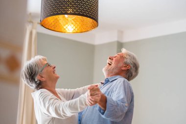 Neşeli aktif yaşlı emekli romantik çift oturma odasında gülerek dans, mutlu orta yaşlı karısı ve yaşlı koca evde eğlenmek, gülümseyen yaşlı aile dedesi birlikte bağ rahatlatıcı