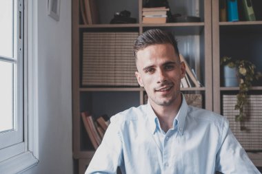 Evde eğlenirken gülümseyen genç bir erkeğin portresi. Çekici beyaz adam bağımsız çalışıyor kameraya bakıyor ve poz veriyor..