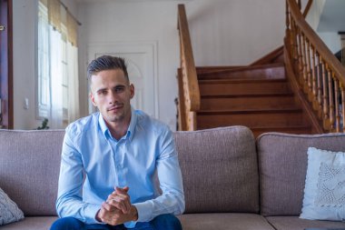 Mutlu bir milenyum erkeğinin portresi evde dinlenen kameraya bakıyor. Uzayı kopyala Dairedeki koltukta oturan kendine güvenen adam fotoğraf çekiyor. Kapat.