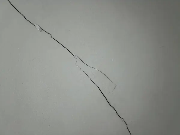 Çatlamış bir duvar yüzeyinde hasar ve yıpranma izleri görülüyor. Ev ortamında onarım ve bakım gereksinimleri vurgulanıyor.