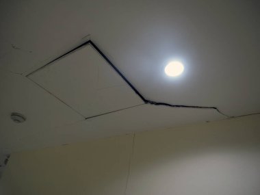 Görünür çatlak ve arızalı lamba armatürüne sahip bir tavan, olası yapısal sorunları gösteriyor. sahne ihmal duygusunu taşır ve gereksinim duyar