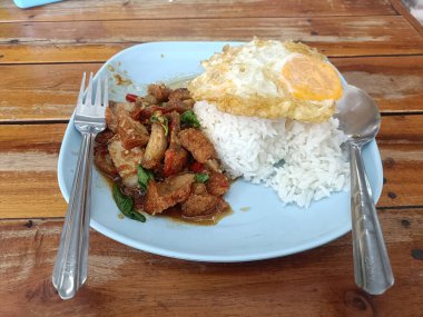 Bir tabak kızarmış domuz, fesleğenli, güneşli, pirinçli yumurta leziz ve davetkar görünüyor. Lezzetli ve doyurucu bir yemek.