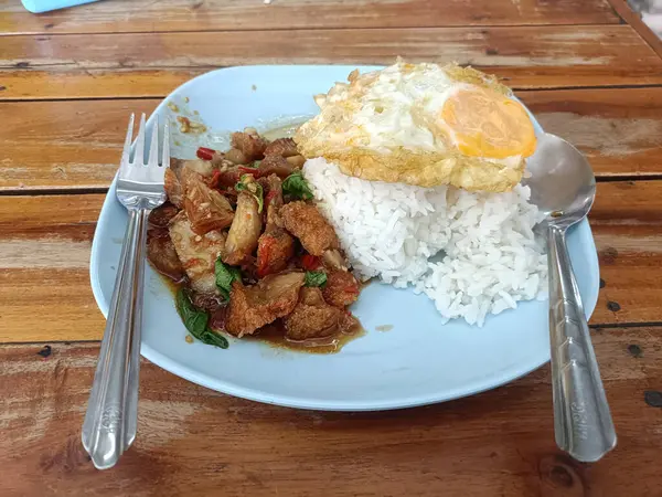 Bir tabak kızarmış domuz, fesleğenli, güneşli, pirinçli yumurta leziz ve davetkar görünüyor. Lezzetli ve doyurucu bir yemek.