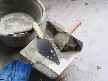 Yerde bir çimento ve alet yıpranmış görünüyor ama gri renk paleti ustalık ve kararlılık hissi yaratıyor.