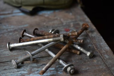 Paslı ve temiz metal cıvata ve vidaların toplanması eskimiş ahşap zemin üzerine saçılmış, koyu arkaplan ile kontrast oluşturarak donanım görünümünü ve yıllanmış ve kullanılan