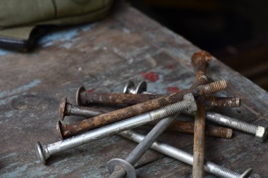 Eski ve paslı çiviler ve cıvatalar eski ahşap yüzeylere saçılmış, ihmal ve yaşlanma hissini taşralı ve endüstriyel hislerle iletiyor.