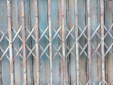 Çapraz desenli paslı metal kapı ve eskimiş mavi boya. Yaş ve elementlere maruz kalma belirtileri gösteriyor. Dokulu ve endüstriyel görünüm yaratıyor.