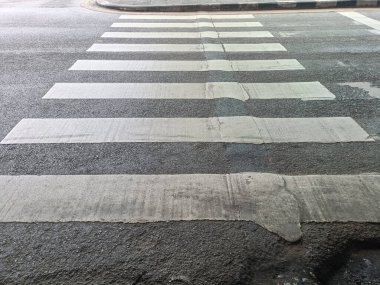 Gri asfalt yol yüzeyinde beyaz yaya geçidi şeritleri geçiş için güven hissi verir.