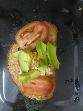 Avokado ve domatesli tost, yumurtalı tam tahıllı ekmek, taze kahvaltı, canlı yeşil avokado ve kırmızı domates dilimleri.