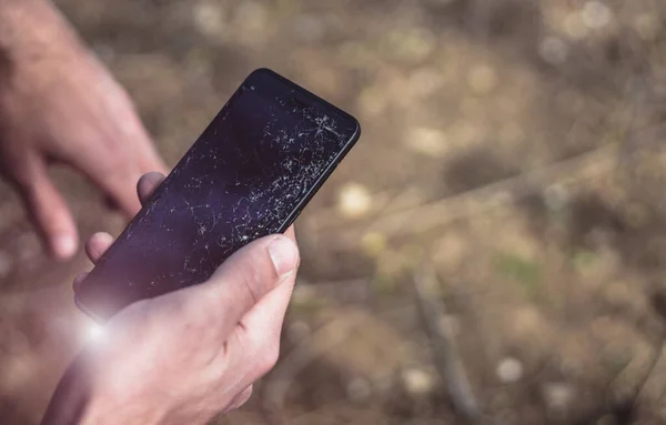 Dışarıda akıllı telefonu bozuk bir adam var. Erkek el ele tutuşurken cep telefonu açık havada kırılmış. Birçok çatlak ve küçük cam parçalarıyla LCD dokunmatik ekran. Metin ve telefon onarımı için boşluk kopyala.