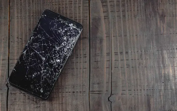 Eski ahşap masada kırık dokunmatik ekranlı mobil akıllı telefon. Bir sürü çatlak ve küçük cam parçaları olan LCD. Boş alanı, üst görünümü, telefon tamir kavramını kopyala.
