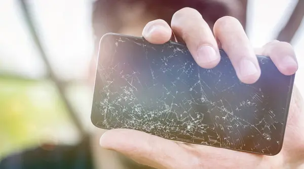 Elinde bozuk bir akıllı telefon tutan adam, aşırı yakın plan. Erkek el, parçalanmış cep telefonu gösteriyor. Hasarlı LCD dokunmatik ekranda bir sürü çatlak ve küçük cam parçaları var. Ön görünüş, telefon tamir konsepti.